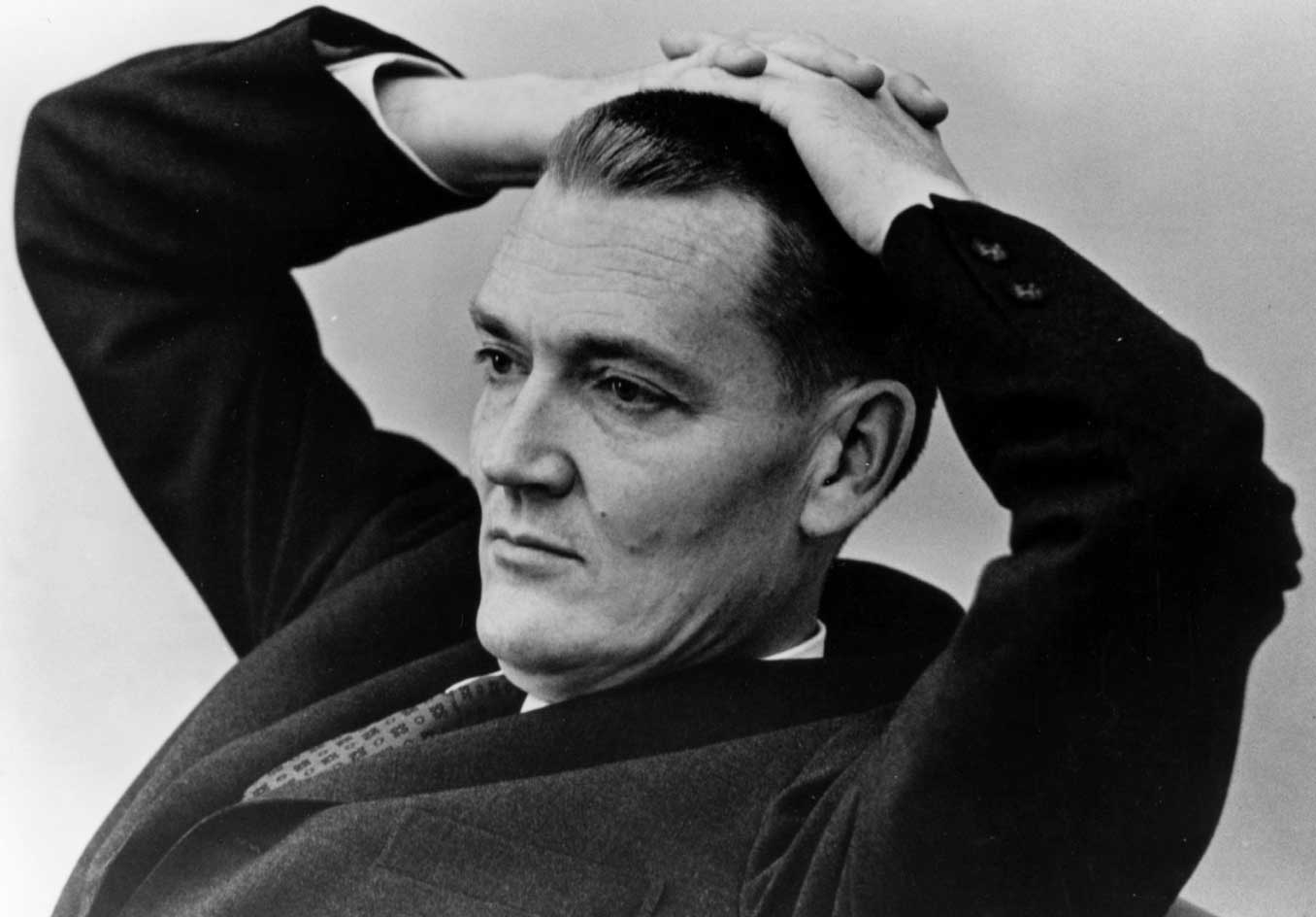 A young Jack Bogle reclines in a contemplative pose with his hands on his head. 