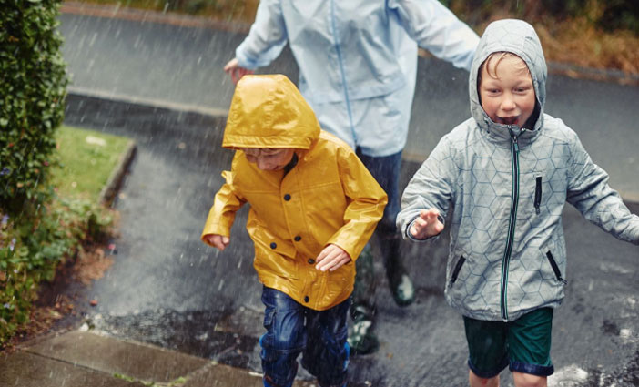 Two children wearing raincoats run through the rain.