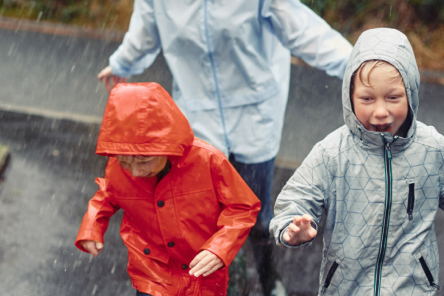Three children in bright raincoats run through the rain.