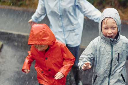 null Three children in bright raincoats run through the rain.
